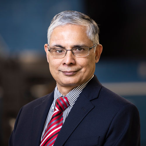A headshot of Gurdip Singh, dean of the school of computing at Mason, wearing a navy blue suit, striped red tie, and glasses