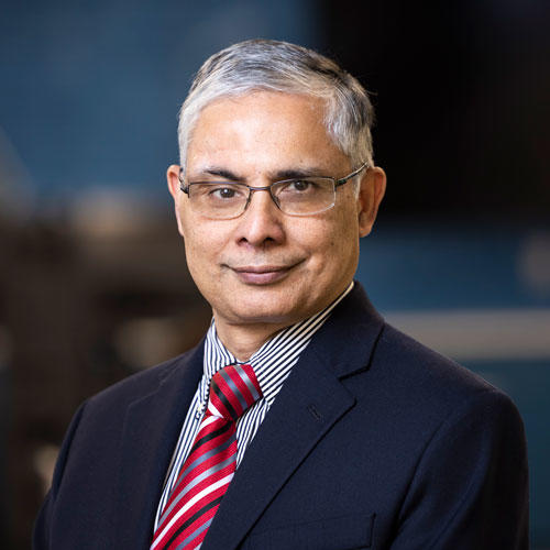 A headshot of Gurdip Singh, dean of the school of computing at Mason, wearing a navy blue suit, striped red tie, and glasses